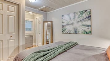 A bedroom with a bed, a green knitted blanket, a painting on the wall, and a door leading to another room.