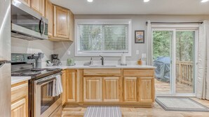 A kitchen with wooden cabinets, a stainless steel refrigerator, a built-in oven, a sink, and a window with blinds. - Mt Air Motel (Welches)