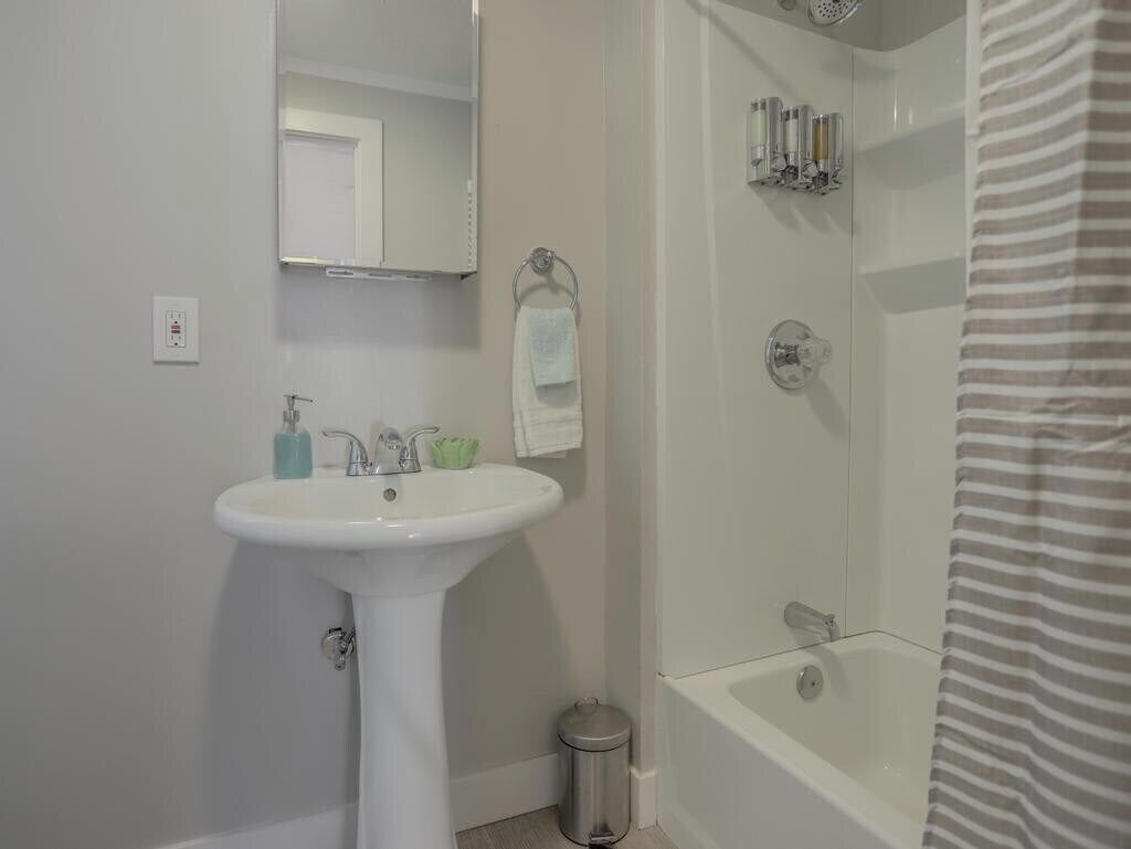 A bathroom with a pedestal sink, a mirror, a shower with a glass door, and a striped shower curtain.