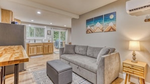 A modern living room with a grey sofa, a wooden dining table, and a small side table with a lamp. - Mt Air Motel (Welches)