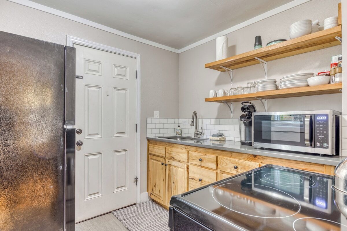 A kitchen with a stainless steel refrigerator, a microwave, a stove, wooden cabinets, and a white door.