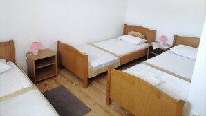 Ein Zimmer mit drei Holzbetten, jeweils mit einer weißen Matratze und einem kleinen Nachttisch mit einer rosa Lampe.