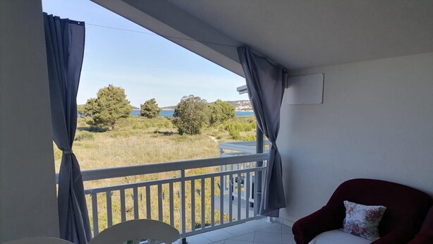 Ein Balkon mit Tisch und Stühlen, ein roter Sessel und Blick auf eine Rasenfläche und Bäume.