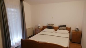 Un dormitorio con una cama de madera, dos mesitas de noche con lámparas, un ventanal con cortinas y una silla roja.