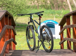 Un vélo est garé sur un pont en bois, et une tente est visible à l’arrière-plan.