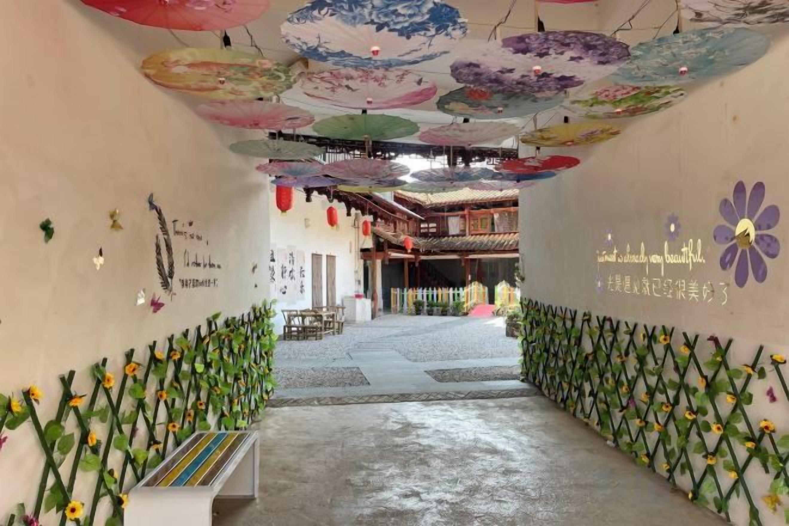 Un pasillo interior con estilo arquitectónico tradicional, que presenta un techo con sombrillas colgantes y una pared con diseño floral.