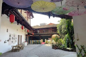 Ein Innenhof mit traditioneller Architektur, darunter ein Ziegeldach und Holzbalken, umgeben von Grünpflanzen und Kübelpflanzen.