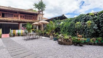 Un patio con un edificio tradicional, un camino de piedra y diversas plantas en macetas.