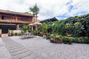 Un patio con un edificio tradicional, un camino de piedra y diversas plantas en macetas.