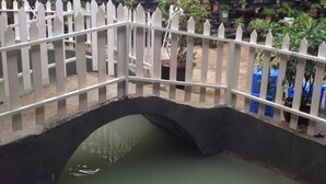 A white picket bridge over a water channel with a stone wall on one side and potted plants in the background. - Puzhehei Qingshui Lianyi Boutique Inn (Qiubei)
