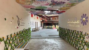 A corridor with a traditional architectural style, featuring a wooden structure in the background and a wall adorned with sunflowers and a decorative ceiling. - Puzhehei Qingshui Lianyi Boutique Inn (Qiubei)