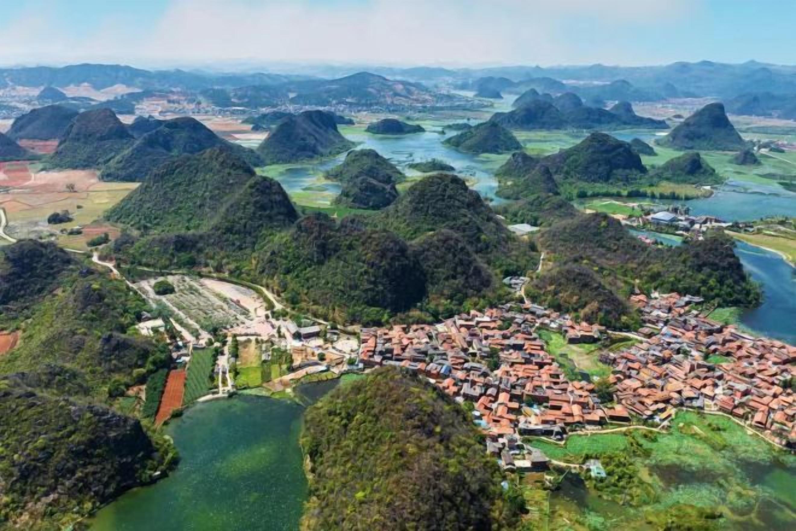 An aerial view of a town with a river, surrounded by hills and greenery.