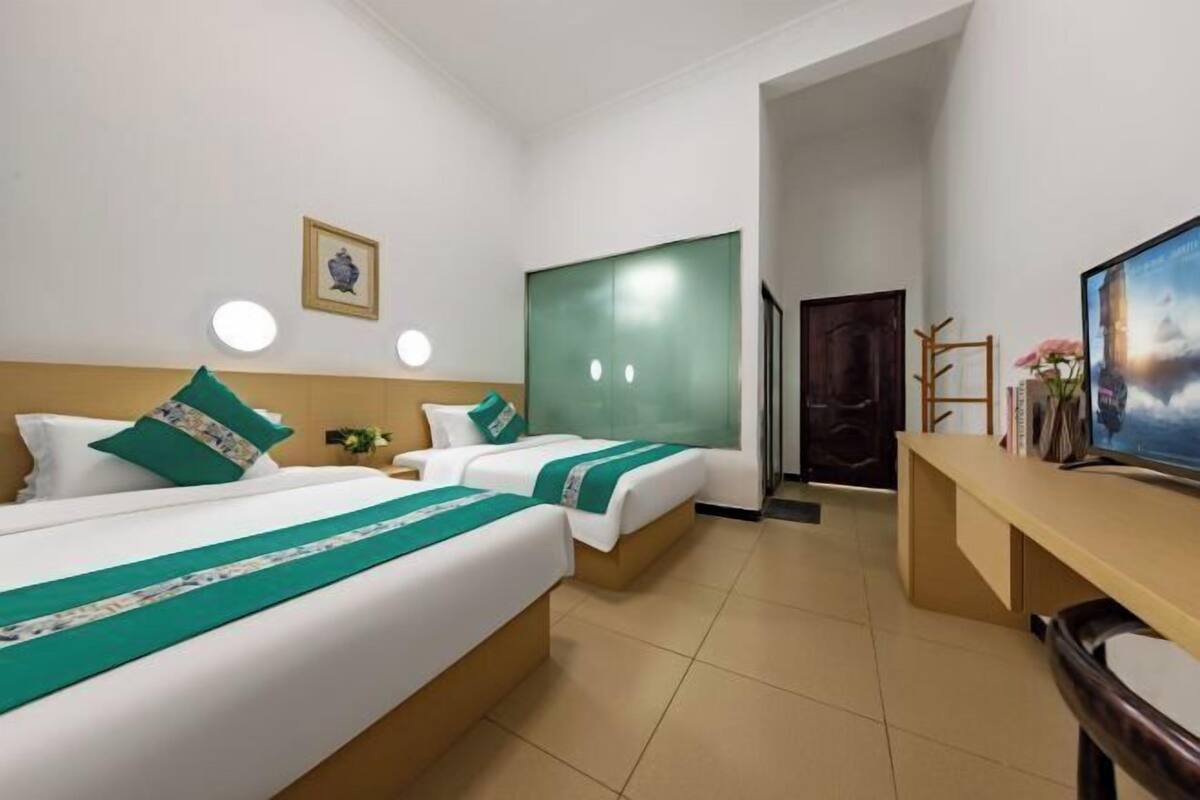 Une chambre d’hôtel avec deux lits, un bureau, une chaise, un tableau et une porte donnant sur une autre pièce.