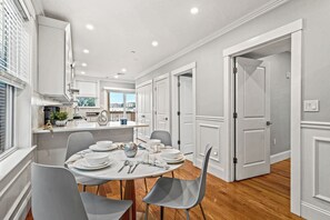 A modern kitchen with a dining area, featuring a round table with chairs, a built-in island, and a view of the city through large windows. - 3-bedroom apartment in charming Boston/ Near Train (Boston)