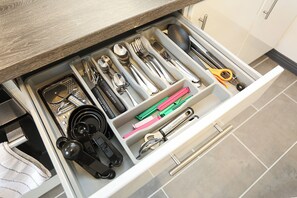 Eine Küchenschublade mit Besteck, darunter eine Reibe, Messbecher und ein Messerset.
