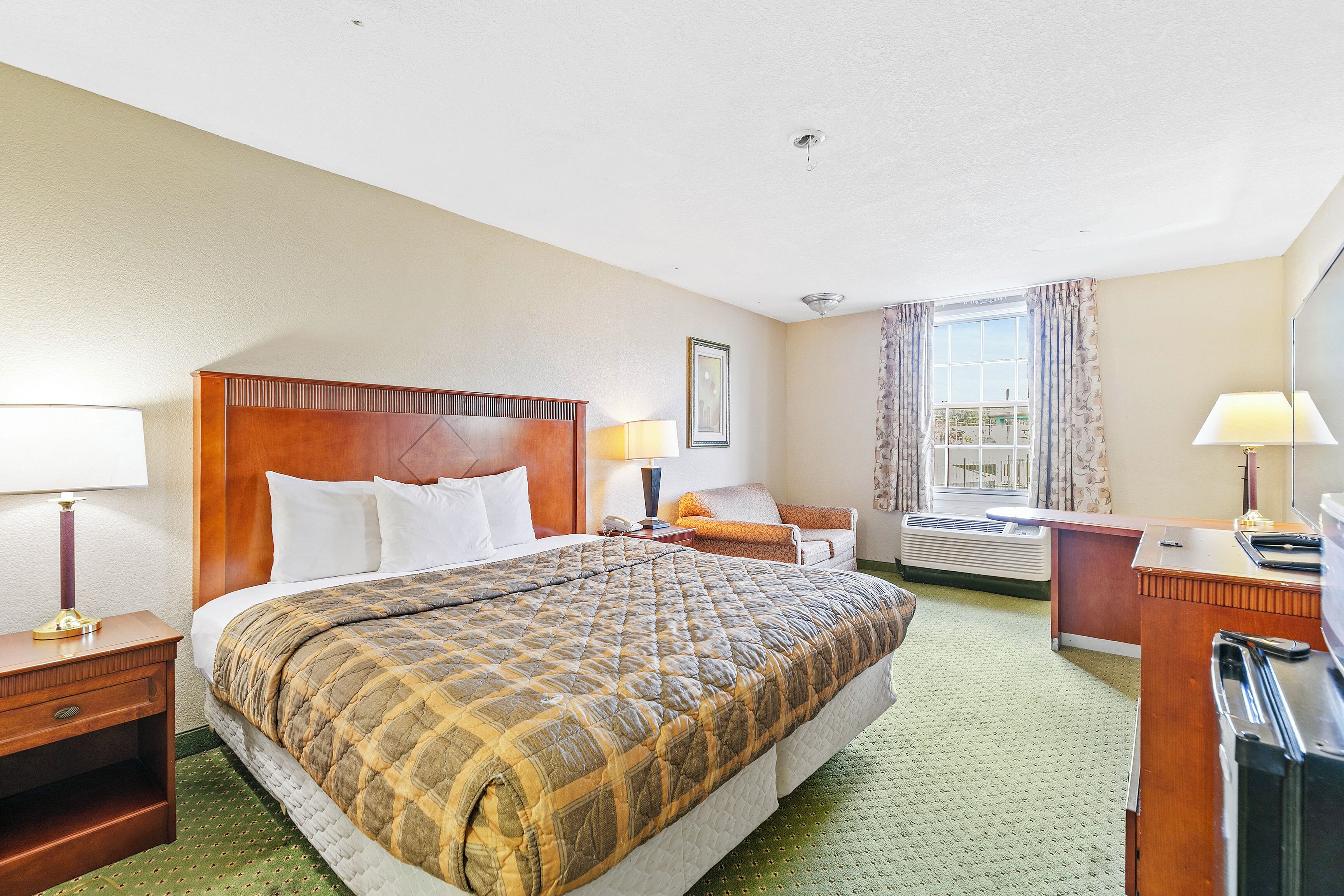 Habitación de hotel con una cama grande, un escritorio con computadora, una silla, una ventana con cortinas y un equipo de aire acondicionado.
