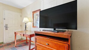 A hotel room with a wooden desk, a flat-screen TV mounted on the wall, a lamp, and a door. - Moonlight Inn Hotel O Hattiesburg, MS (Hattiesburg)