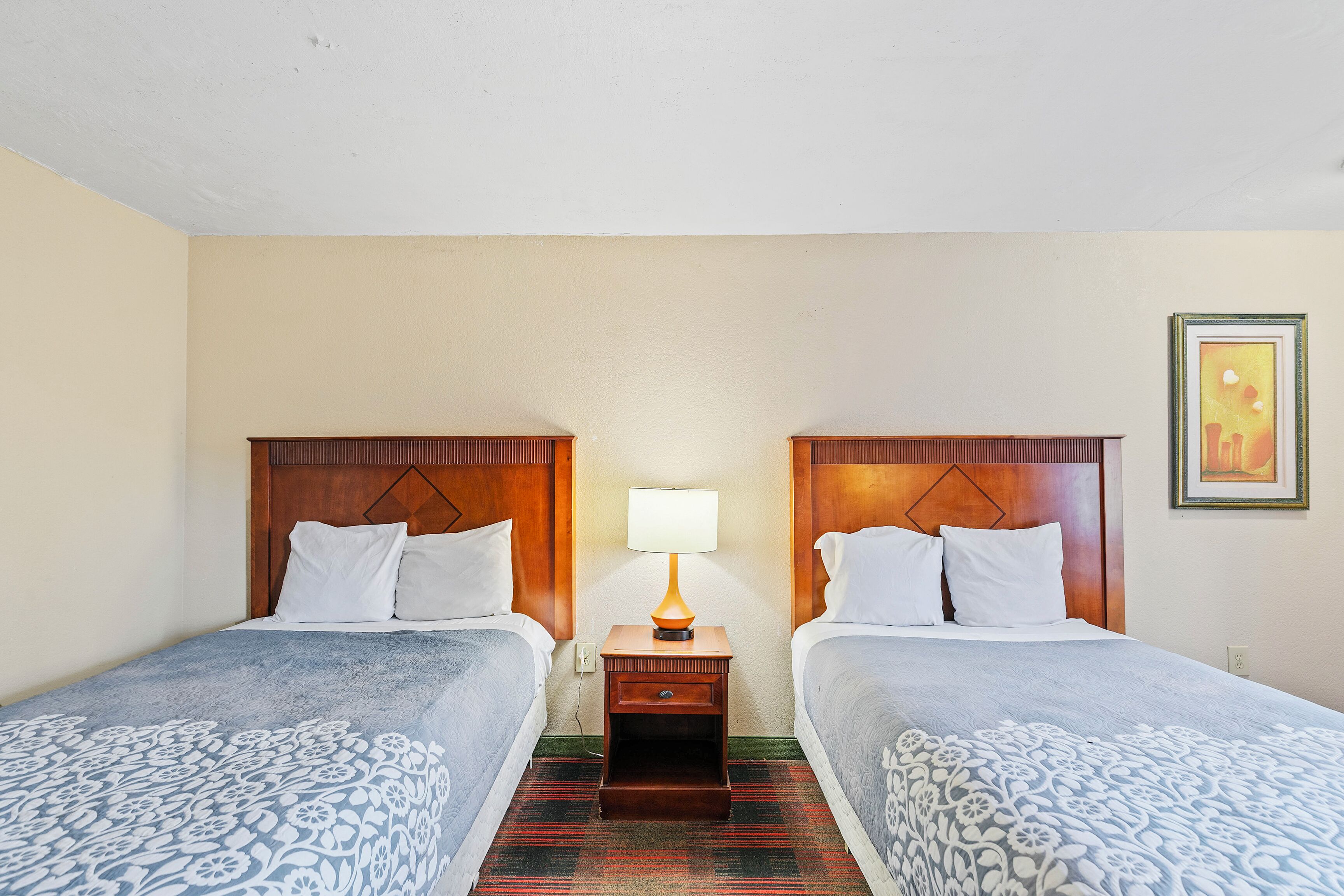 Une chambre d’hôtel avec deux lits, une table de chevet avec une lampe et un tableau encadré au mur.