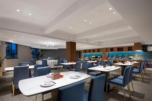 Un comedor moderno con varias mesas y sillas, un área de bar al fondo, y un amplio ventanal que proporciona luz natural.