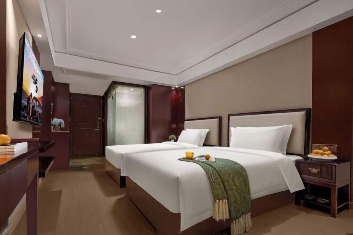 A hotel room with two beds, a TV, a desk, and a small table with fruit.