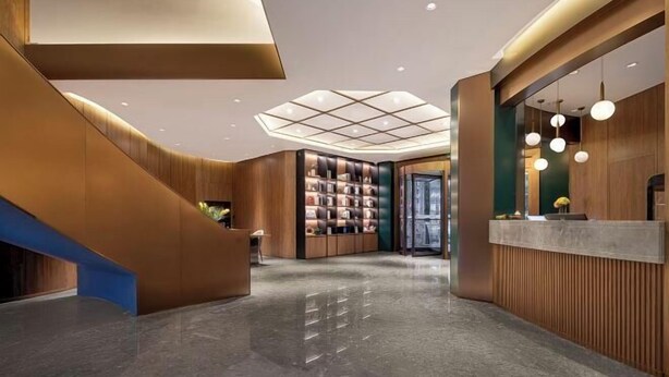 Un moderno vestíbulo de hotel con una escalera central, un mostrador de recepción y una puerta de cristal que da a la entrada.