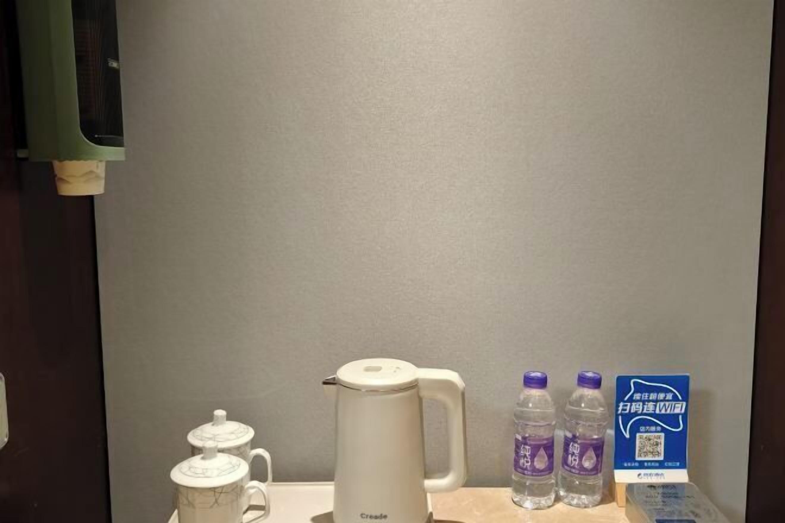 Habitación de hotel con cafetera blanca, dos botellas de agua y un cartel con un código QR.