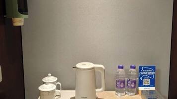 Habitación de hotel con cafetera blanca, dos botellas de agua y un cartel con un código QR.