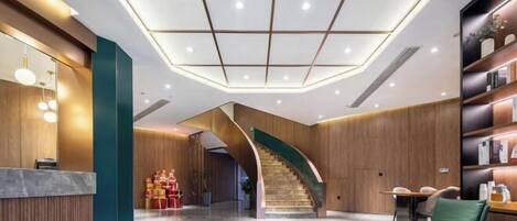 Eine moderne Lobby mit einer geschwungenen Treppe, einem Empfangsbereich und einer Sitzecke.
