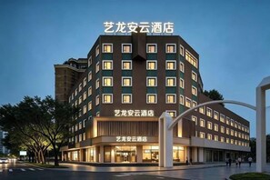 Un hotel de varios pisos con un diseño moderno, que presenta una entrada destacada y una estructura curva a la derecha.