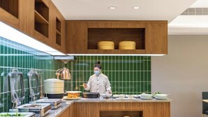 Una cocina moderna con un chef preparando comida, armarios de madera y un salpicadero de azulejos verdes.