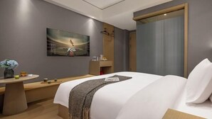 Una habitación de hotel moderna con una cama grande, una mesita de noche con un jarrón de flores, un televisor montado en la pared y una ventana con cortinas.