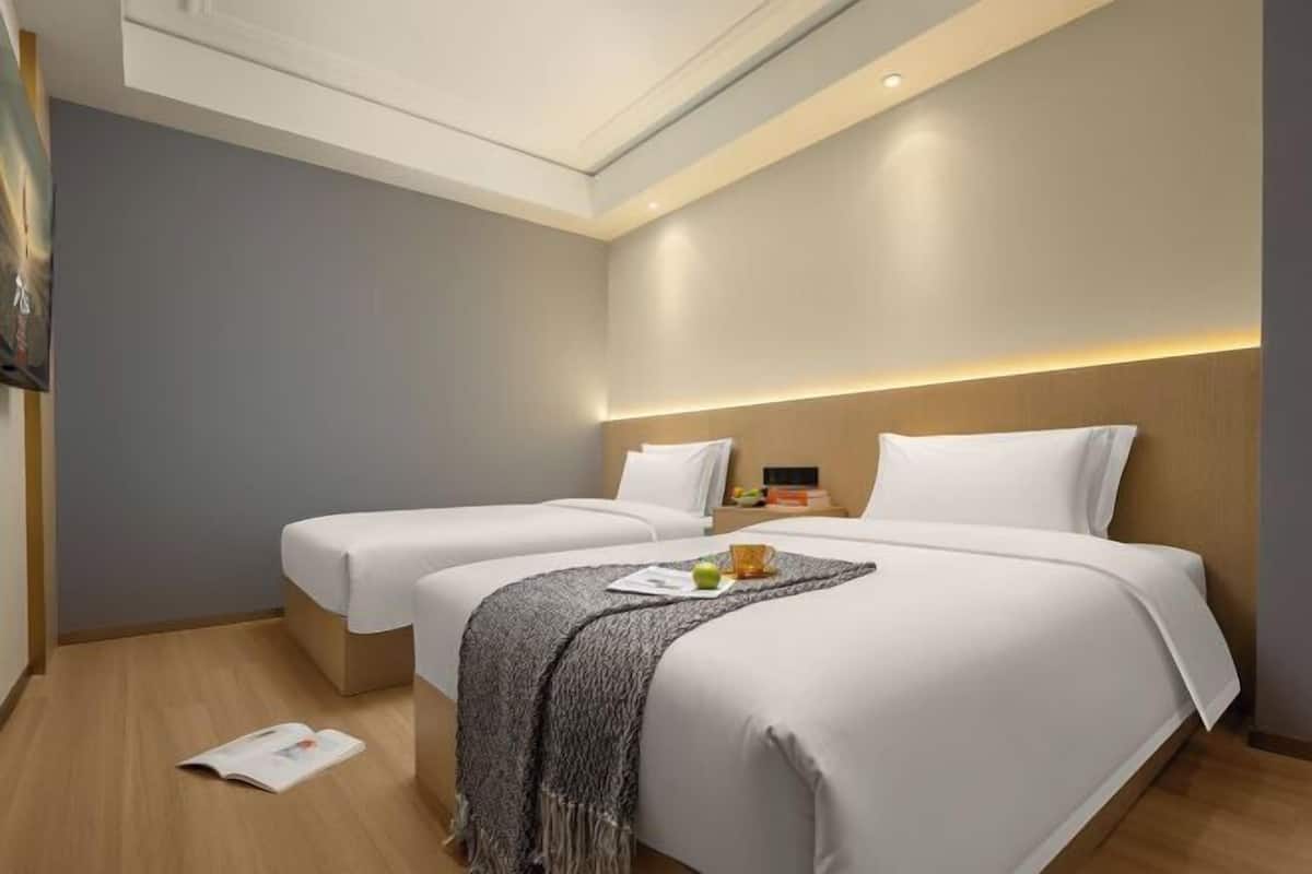 A hotel room with two beds, a ceiling light, and a small table with a cup and apple.