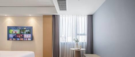 Une chambre d’hôtel moderne avec un lit, une petite table ronde ornée d’un vase et une grande fenêtre avec des rideaux.
