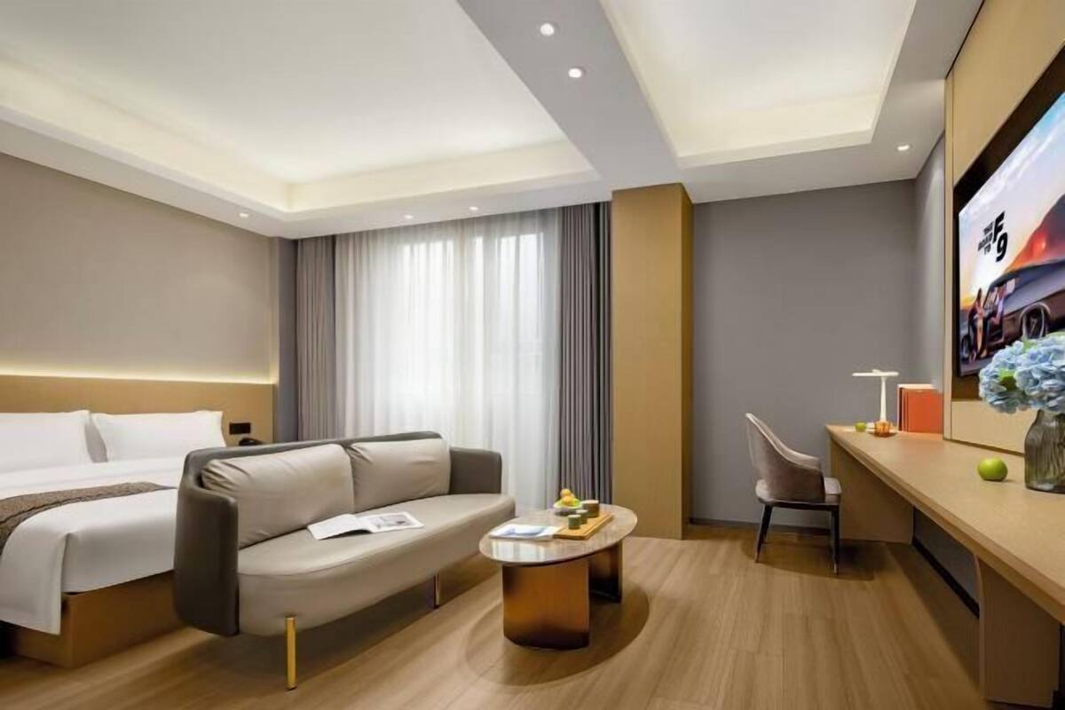 A modern hotel room with a bed, a sofa, a desk, and a chair.