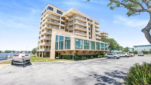 A multi-story building with balconies, a parking lot, and a boat in the foreground. - Compass Point 201 Pet-friendly for fee Boat Ramp (Gulf Shores)