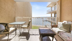 A balcony with a table and chairs, a wicker sofa, and a view of the water. - Compass Point 201 Pet-friendly for fee Boat Ramp (Gulf Shores)