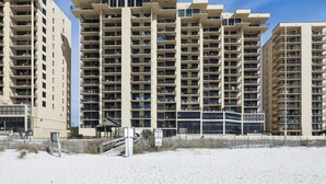 Un hôtel de grande hauteur doté de nombreux balcons, une plage de sable en premier plan et un ciel bleu dégagé.
