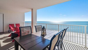 A balcony with a wooden table and chairs, a lantern, and a view of the ocean. - Windward Pointe 1104 Amazing Views A Amenities (Orange Beach)