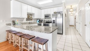 Una cocina con gabinetes blancos, encimera de granito, electrodomésticos de acero inoxidable y taburetes de bar de madera.
