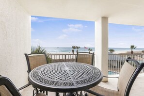 Una mesa redonda con diseño calado, rodeada de sillas con asientos de mimbre, en un balcón con vista a la playa y al océano.