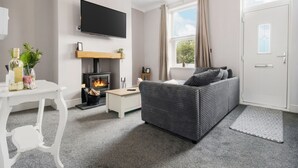 A modern living room with a fireplace, a sofa, a TV, and a dining table. - Cosy Green End Retreat (Wakefield)