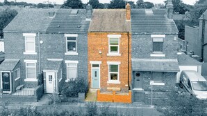 A residential area with houses, including a distinct red brick house with a front door and windows, surrounded by other houses. - Cosy Green End Retreat (Wakefield)