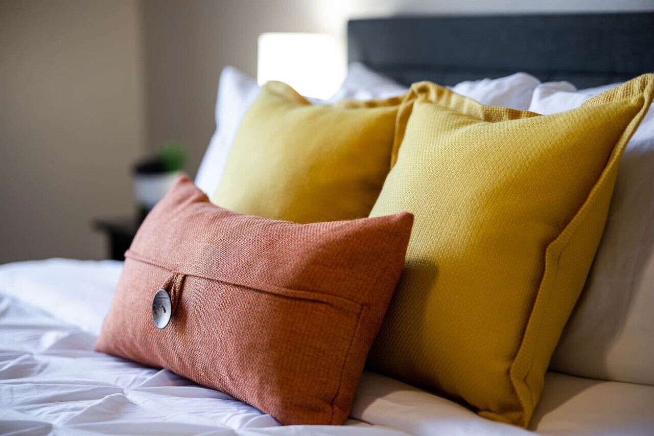A bed with white bedding and two pillows, one in a rust color and the other in a mustard yellow.