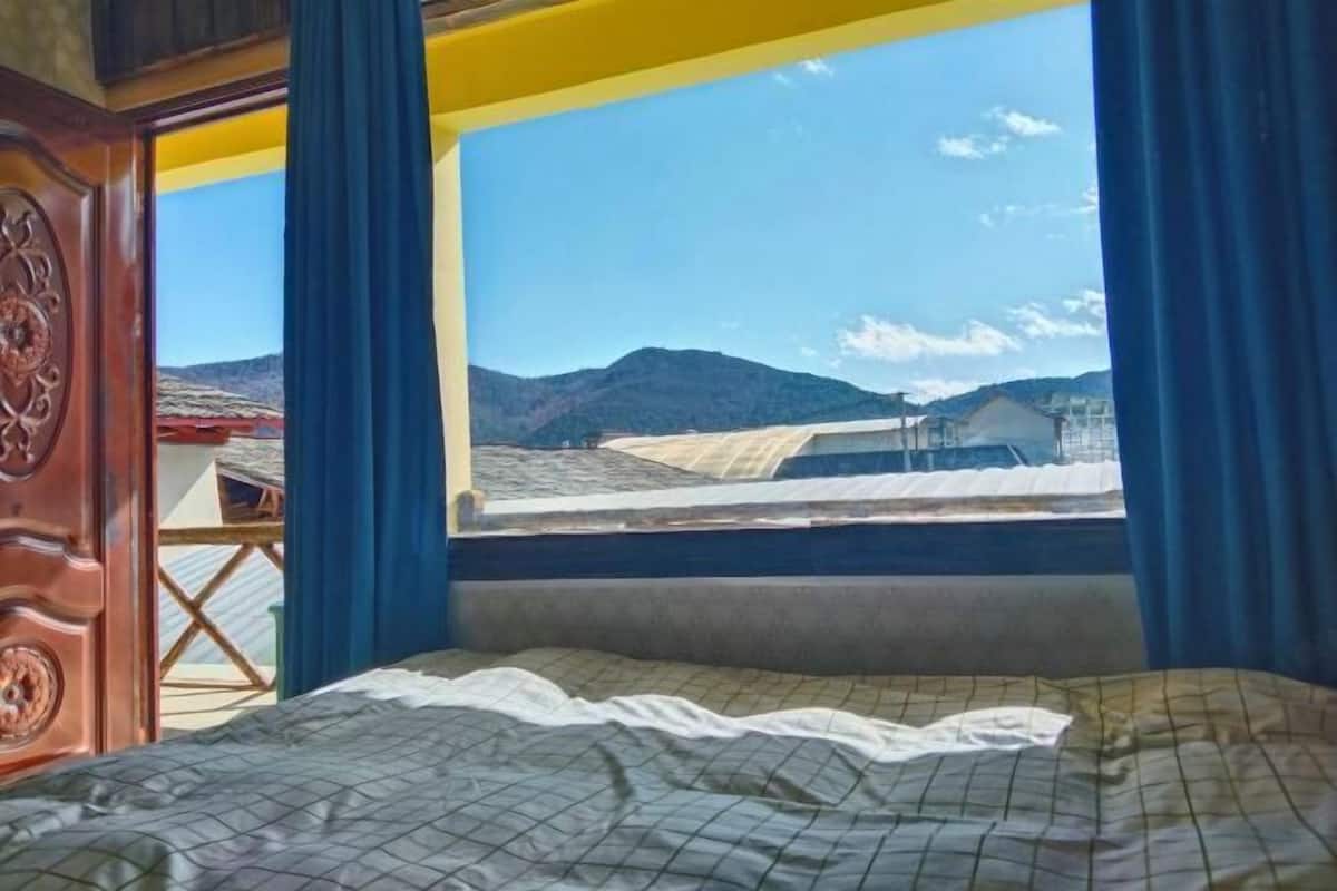 Une chambre avec un lit, une fenêtre avec des rideaux et une vue sur les montagnes.