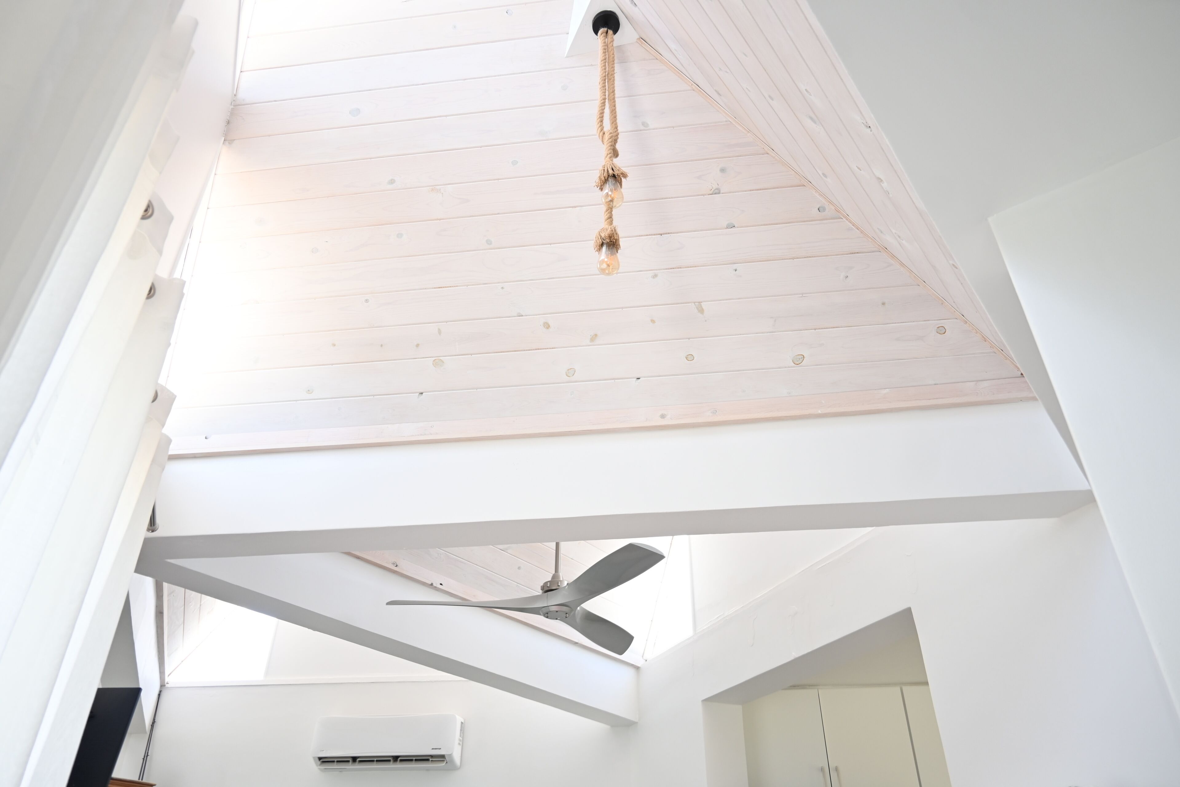 A high ceiling with a rope light fixture, a ceiling fan, and an air conditioning unit in a modern, white-walled room.