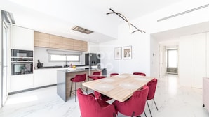 Una cocina moderna con armarios blancos, una isla central y sillas rojas alrededor de una mesa de madera.