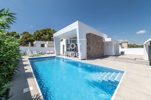A modern poolside area with a clear blue pool, white walls, and a stone structure. - Villa Coral, chic coastal design, saltwater pool - by OYOOSTAYS (Torrevieja)