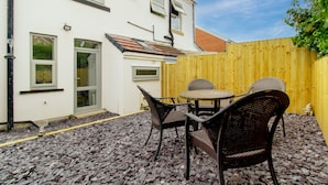 A patio with a table and chairs, a wooden fence, and a white building with windows and a door. - Lovely Lawns Lane (Carr Gate)