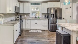 Una cocina con armarios blancos, un refrigerador de acero inoxidable, un horno empotrado y una cafetera.