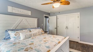 Un dormitorio con una cama, ventilador de techo, una puerta y una pared con un letrero decorativo.